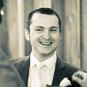 man smiling, wearing grey coat and white dress shirt 