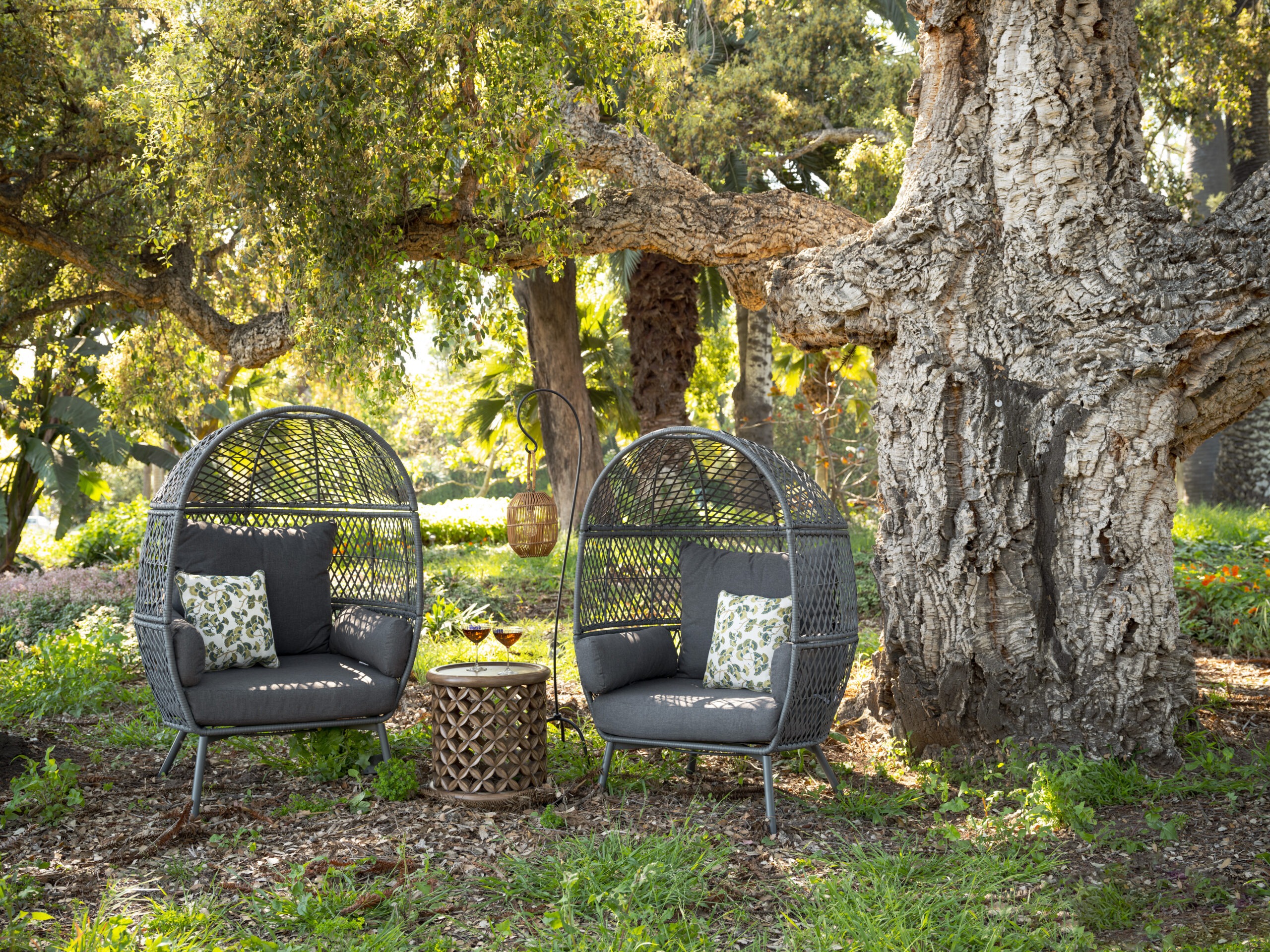 One of The Steward's gathering moments. Two outdoor chairs stand under a tree. In between them is a table with two wine glasses.