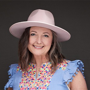 woman smiling, wearing wide-brimmed hat and sequined blue shirt