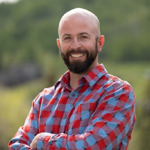 man with crossed arms and blue and red plaid shirt smiling