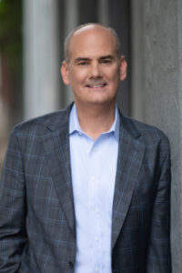 man wearing blue suit, leaning against wall