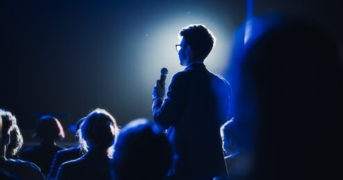 Accor meetings survey story featured image of a man giving a speech to a crowd against blue light, credit: Shutterstock