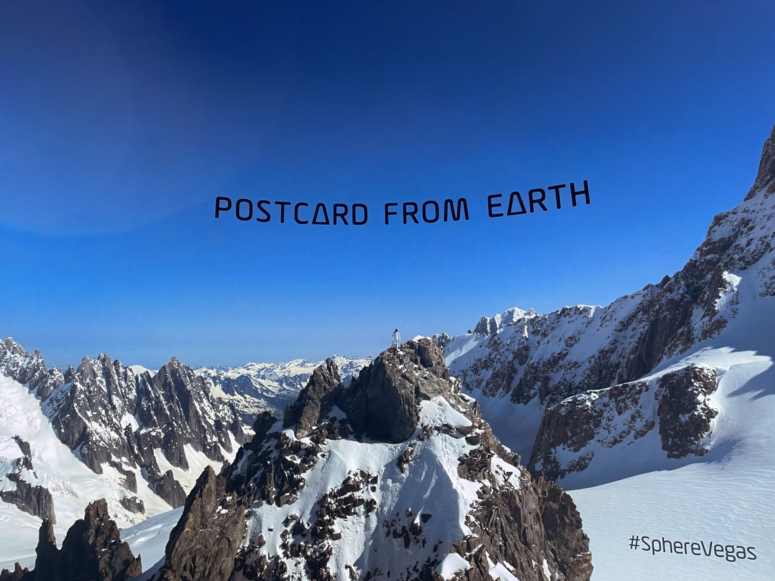 screen that reads "postcard from earth" among snowy mountains
