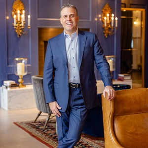man in blue suit and grey shirt smiling