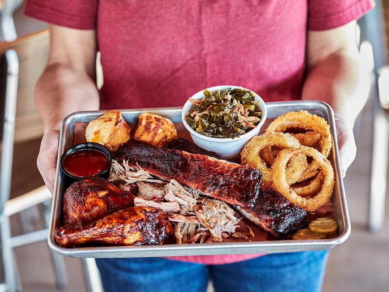 person holding plate of ribs, chicken, onion rings