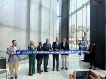 Ribbon cutting at Baird Center Expansion with six people and a blue ribbon.