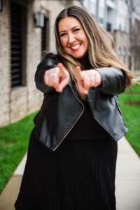 Rachel Sheerin wearing black leather jacket and black dress, pointing at camera