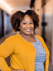 Takia Archer wearing yellow coat and blue shirt