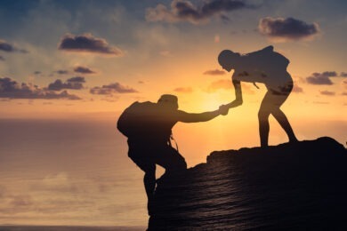 one silhouetted climber helping someone