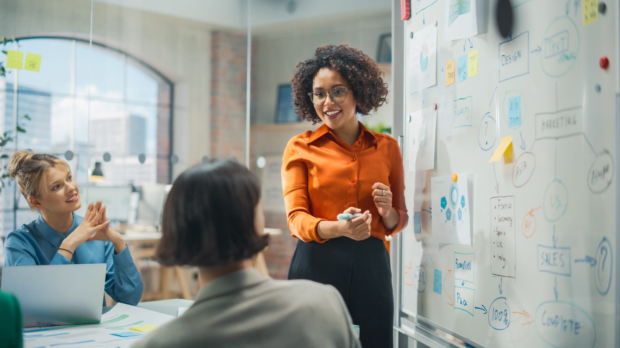 woman writing on board and talking to colleagues