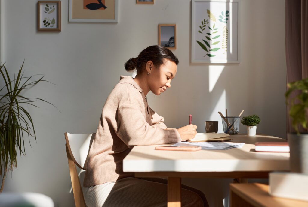 Side view of young African American woman writing in notebook at home