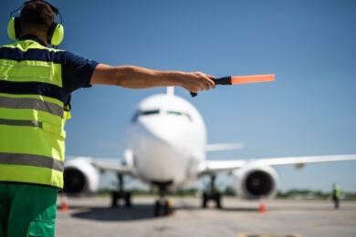 Back view of airport worker meeting aircraft and showing right position for landing