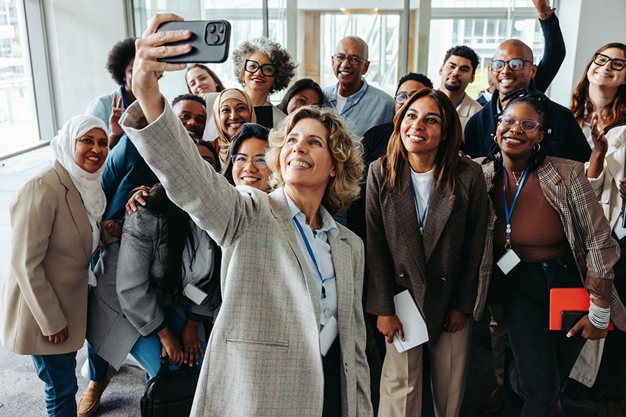 A diverse group of professionals taking a cheerful selfie together during a seminar or workshop. They are smiling and appear engaged. hilton meetings maximizer