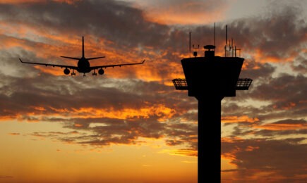 Silhouetted airplane and air traffic control tower at dawn