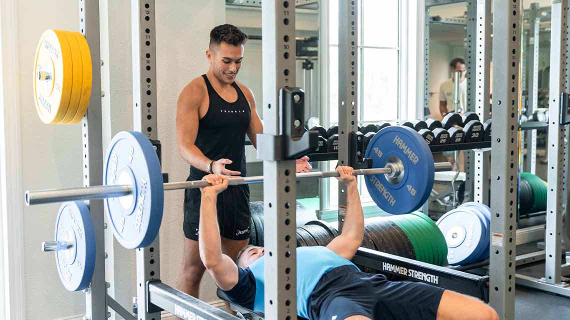 Fitness instructor helping man lift weights